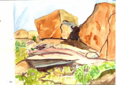 Desert landscape with large orange rock formations, boulders, and sparse green vegetation.